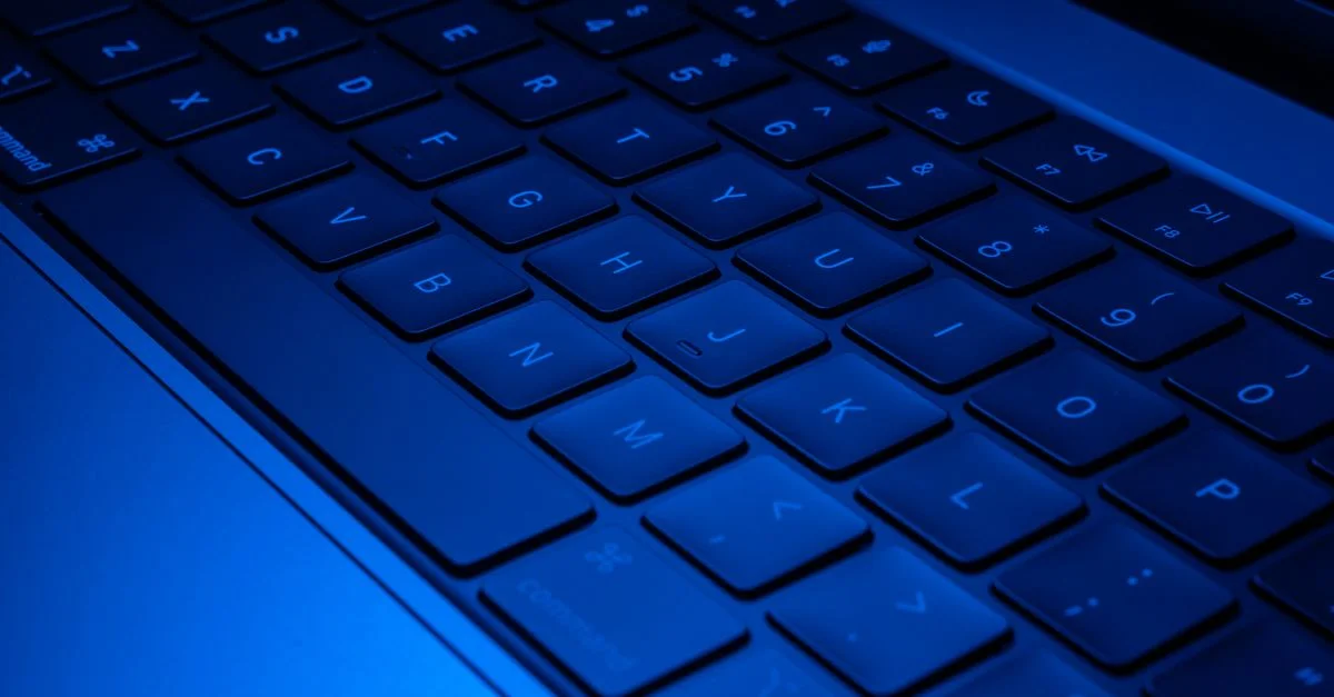 Image en gros plan d'un clavier d'ordinateur portable illuminé par une lumière bleue, mettant en valeur le design technologique moderne.