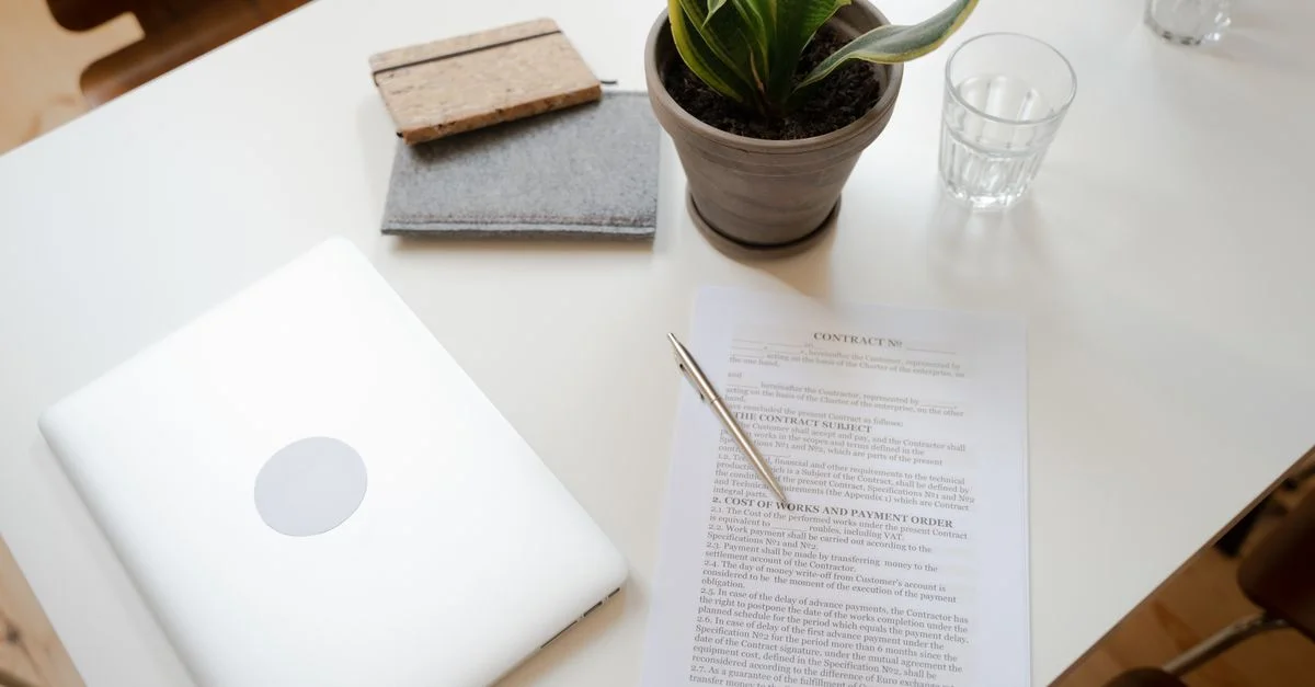 Vue de dessus d'un espace de travail propre avec un ordinateur portable, un contrat et une plante pour la productivité et la concentration.