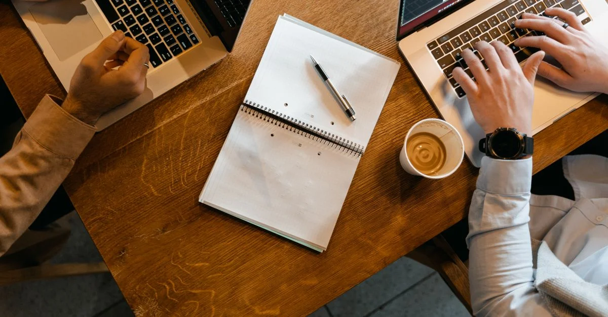 Vue de dessus de collègues utilisant des ordinateurs portables avec des notes et du café sur un bureau en bois.