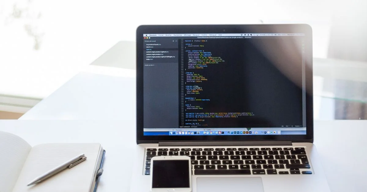 Ordinateur portable ouvert affichant du code sur un bureau avec un smartphone et un carnet, idéal pour l'utilisation en technologie et en affaires.