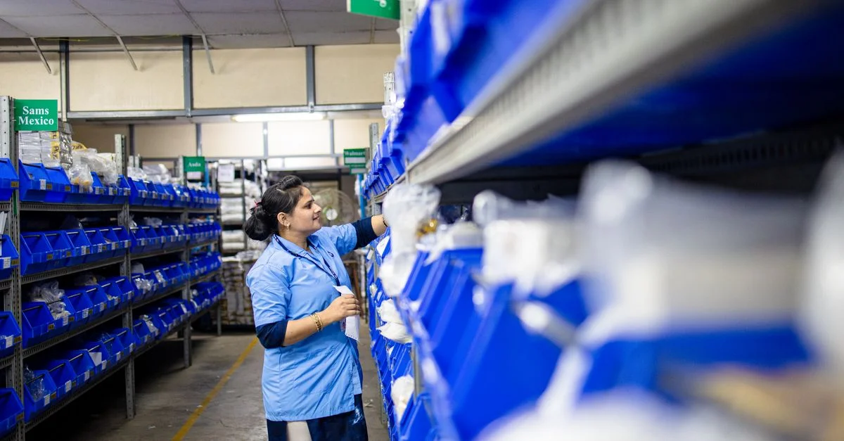 Une femme dans un entrepôt organise les étagères d'inventaire avec des bacs étiquetés.