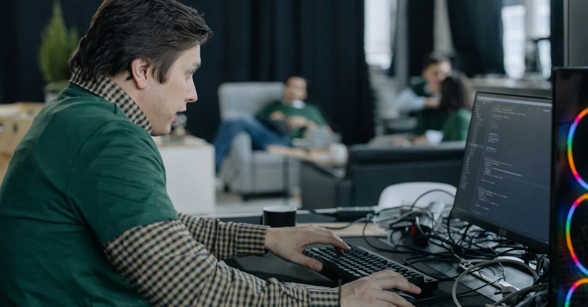 Programmeur masculin se concentrant sur le codage à l'ordinateur dans un environnement de bureau contemporain.