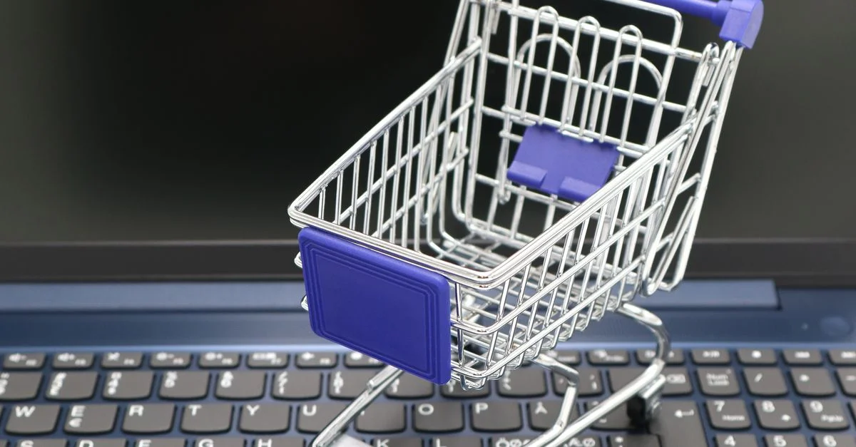 Un mini chariot de course placé sur le clavier d'un ordinateur portable, symbolisant l'achat en ligne et le commerce numérique.