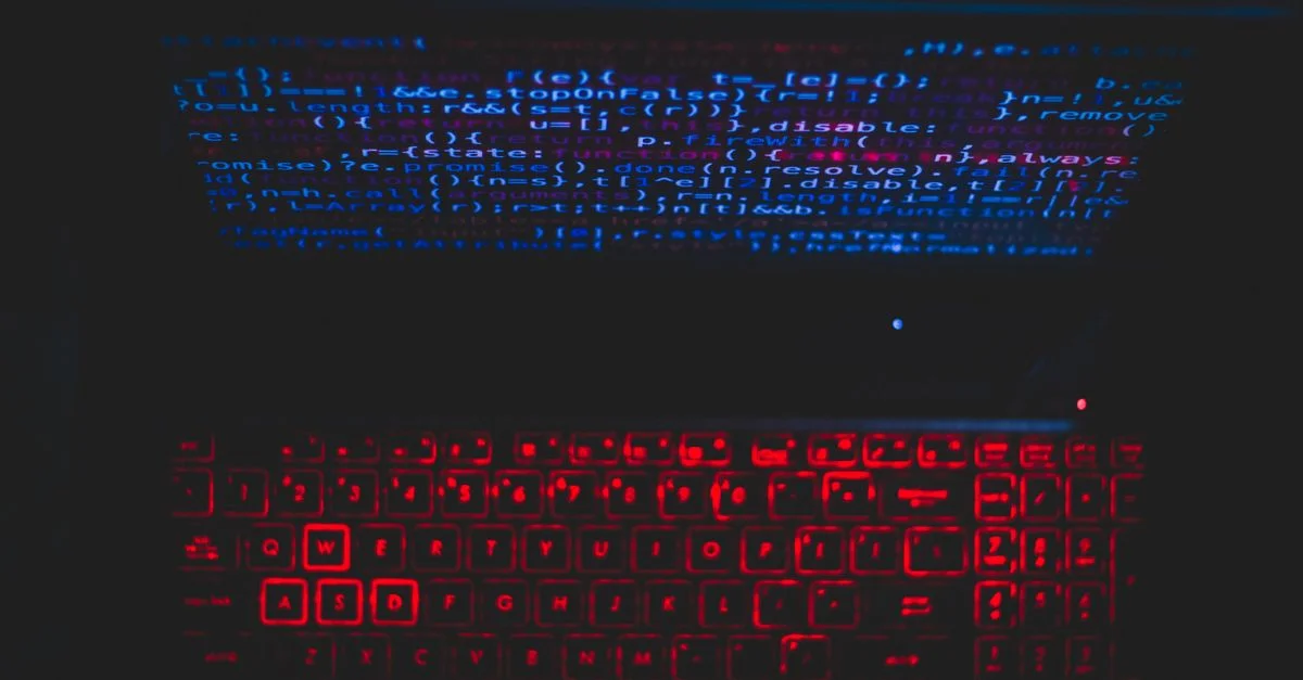 Configuration d'ordinateur portable aux tonalités sombres avec un clavier rouge lumineux et du code à l'écran, idéal pour les passionnés de technologie.