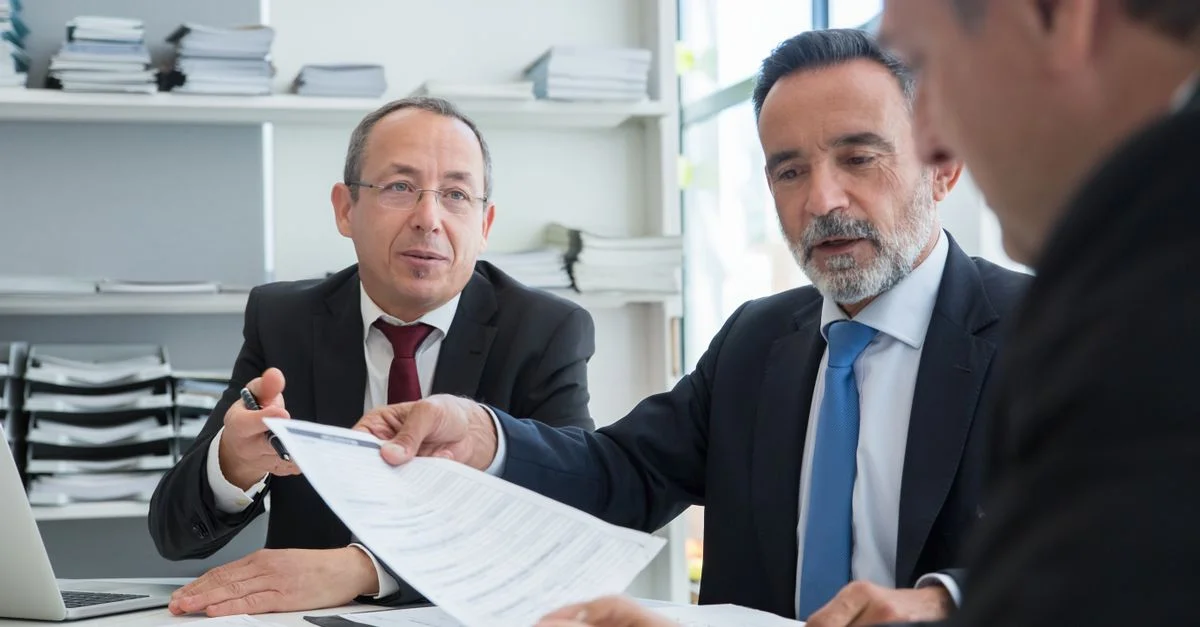 Trois hommes d'affaires discutent de documents dans un cadre de bureau moderne.
