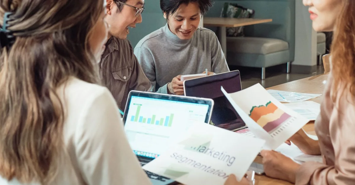 Groupe de collègues discutant des stratégies marketing avec des graphiques et des ordinateurs portables dans un environnement de bureau.