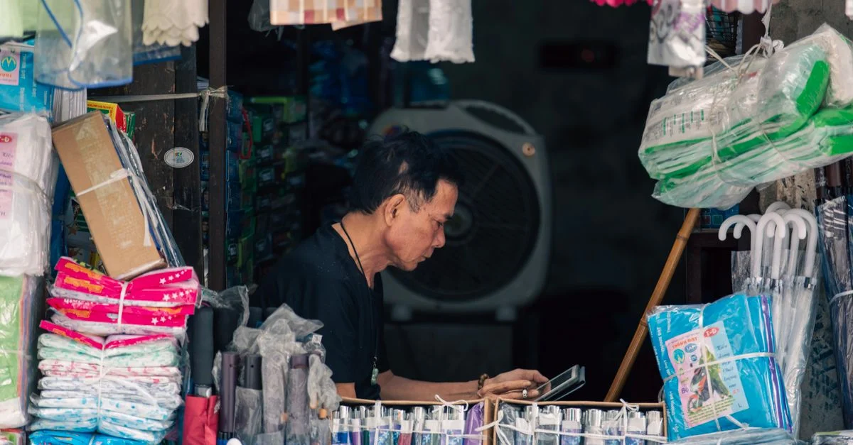 Dans une boutique vietnamienne traditionnelle, un commerçant range des textiles. L'endroit est vibrant et animé, regorgeant de tissus.