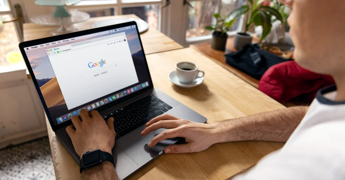 Une personne utilise un ordinateur portable pour naviguer sur Internet. Un cadre lumineux à l'intérieur avec du café sur une table en bois.